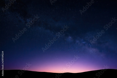 Vast starry sky with a glowing horizon over dark, silhouetted landscape
