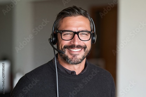 Friendly male customer service representative wearing a headset and glasses smiling at the camera