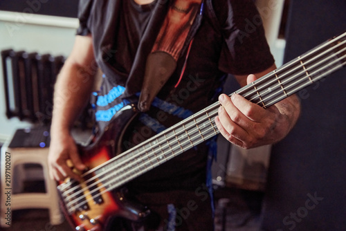 Bild auf Leinwand Bass guitarist playing electric bass in rehearsal studio with warm light