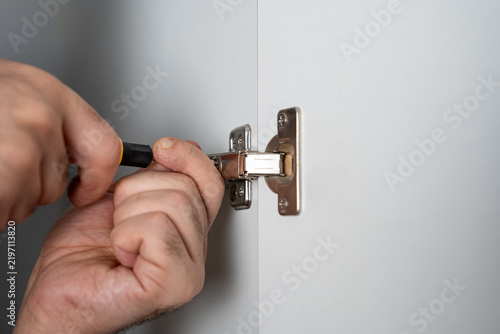 Принти на полотні Close-up of hands adjusting a metal hinge on a wall using a screwdriver