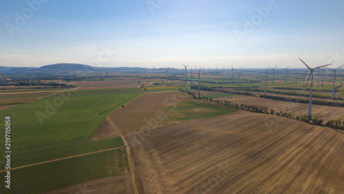 Aerial view of a wind farm with numerous wind turbines standing in vast agricultural fields under a clear blue sky in Hainburg an der Donau, Lower Austria, Austria.