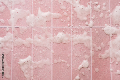 Scattered cleaning foam on pink tiles with straight grout lines in overhead view.