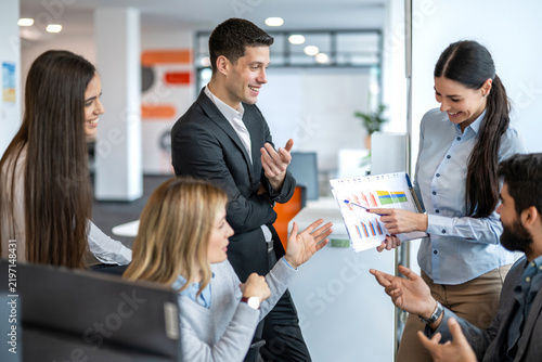 Businesswoman presenting sales report charts to colleagues gathered in modern office