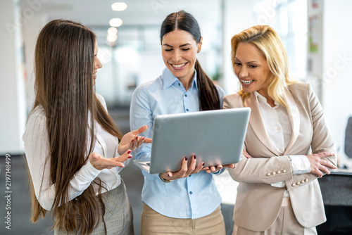 Three smiling businesswomen looking at laptop screen during informal meeting