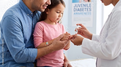 Pediatrician teaching a young girl and her father how to monitor blood glucose levels for the management of juvenile diabetes in a clinic