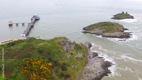 Aerial view of Mumbles Lighthouse situated on a rocky island near the Mumbles Pier, surrounded by the sea and green coastal cliffs in Mumbles, Wales, United Kingdom.