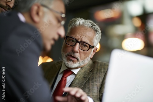 Two mature businessmen in suits looking at a laptop screen during a collaborative meeting time