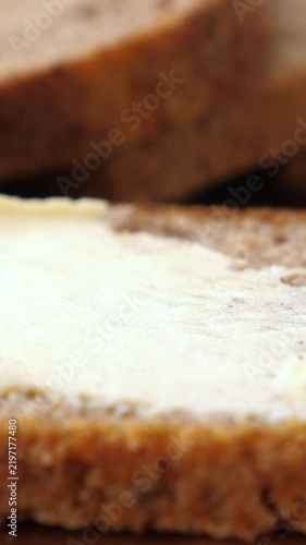 Butter spread on bread slices in close up. Spoon lifts soft butter, then smooths it across toasted bread, creating simple breakfast preparation with warm kitchen light and appetizing texture.