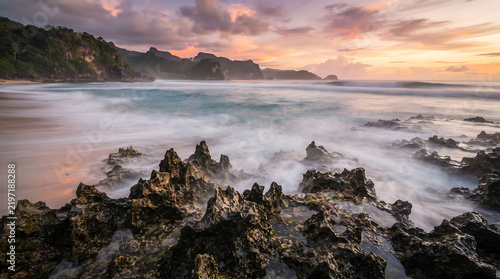 Breathtaking tropical beach sunset with dramatic rocky foreground and motion blur waves