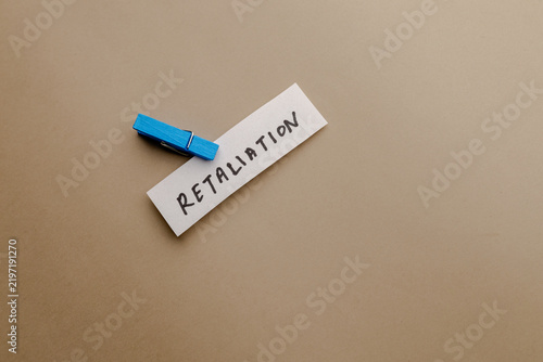 Fotografie Retaliation text written on paper clip with blue peg on beige background, concep
