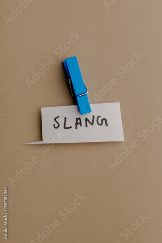 Foto A small white note with hand written word slang attached by a bright blue wooden