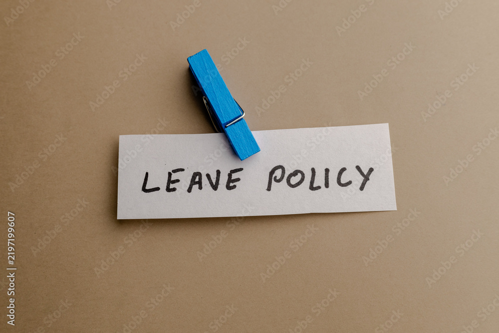 Obraz premium A close up view of a paper note with leave policy text handwritten in black ink attached by a wooden blue clothespin on a brown background