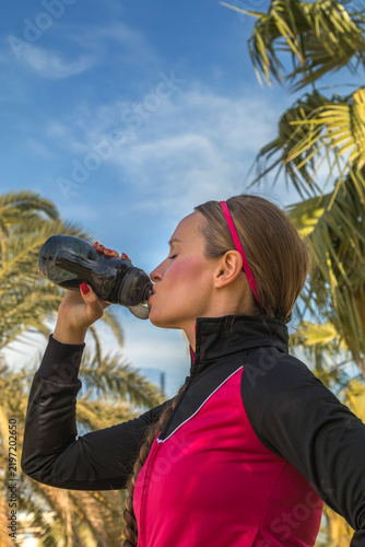 Fotografie Sporty young woman in a track jacket drinking from a sports water bottle