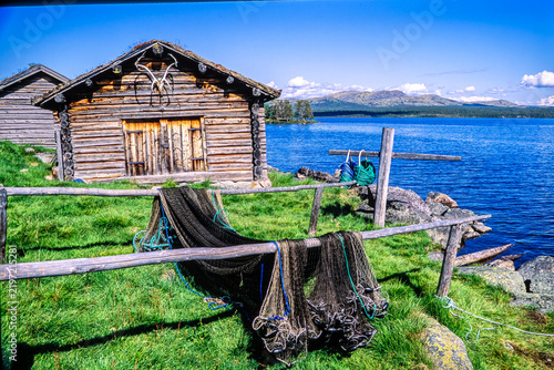 Rural heritage at Sølensjøen. An old log-built fisherman’s hut stands by the water’s edge, decorated with reindeer antlers and framed by drying fishing nets.