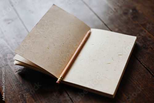Open recycled paper notebook with blank pages and wooden pencil on dark wood, eco stationery