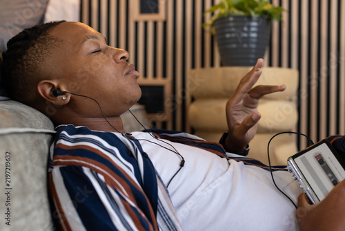 African American man reclining on cushioned sofa, listening with wired earphones to cassette player