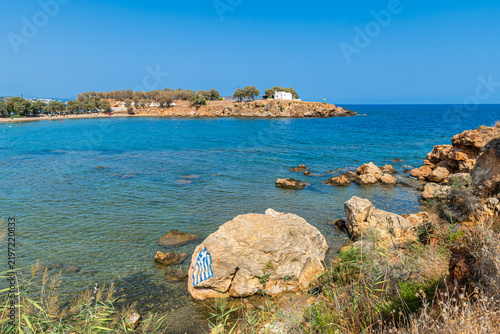 The Chapel of the Holy Apostles at Agii Apostoli beach in Chania, Crete, a historic white orthodox church on a rocky peninsula in summer.