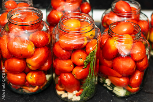 Jars filled with ripe red tomatoes and fresh herbs arranged on a kitchen countertop, showcasing home canning and preservation techniques for seasonal produce