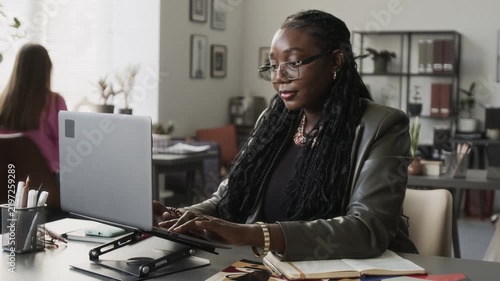 African American young adult woman typing on laptop at workplace desk. Perfect for corporate communication, tech tutorials, and digital business promotions