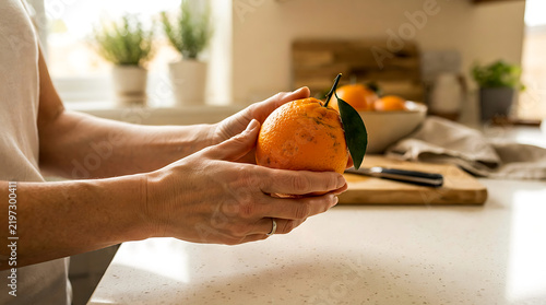 Woman holding a fresh orange in her hands in a bright sunny home kitchen