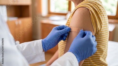 Medical professional applying a bandage to a patient's arm after an injection or vaccination in a clinic setting.