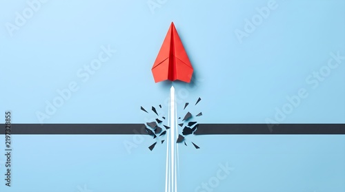Red paper plane breaking through black finish line.