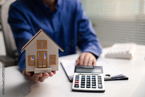 Fotografie Professional holds a house model beside a calculator while reviewing mortgage documents