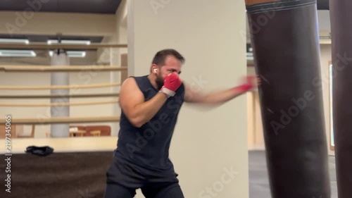 A video of a forty year old man in black sportswear practicing fast kickboxing strike combinations on a heavy bag during a high intensity gym workout session.