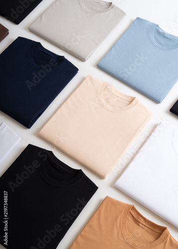 A clean flat lay composition of neatly folded plain t-shirts in various solid colors on a white background.