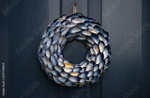Obraz na plátne Handmade maritime wreath crafted from blue mussel shells (Mytilus edulis) hanging on a dark wooden front door in Robin Hood’s Bay, North Yorkshire, England