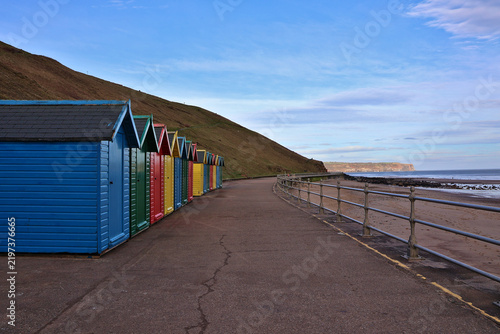 Colourful Whitby Beach Huts on Whitby Beach, North Yorkshire; seaside chalets on coastal promenade, traditional English holiday landmark at base of West Cliff, Whitby, England, UK
