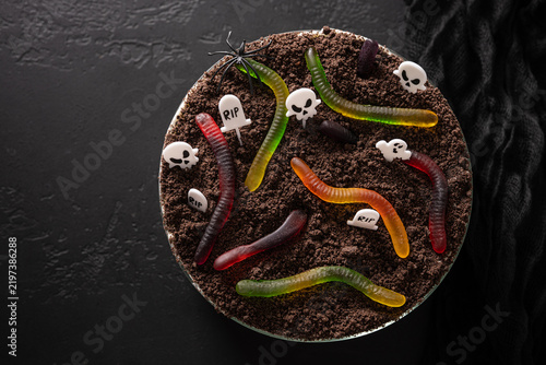Halloween dirt cake decorated as a spooky graveyard with gummy worms, skulls, tombstones and spider on chocolate crumb soil. Top view with copy space.