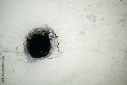 Foto Close up of a dark circular hole in an old concrete wall with cracks and damaged plaster, representing building deterioration, construction defects, repair, renovation, maintenance
