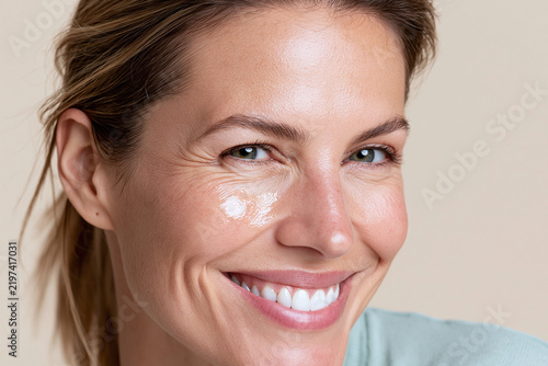 Radiant smiling woman with dewy skin and cheekbone highlight, close up macro portrait showing healthy complexion, natural makeup, toothy smile and light wrinkles conveying warmth and confidence