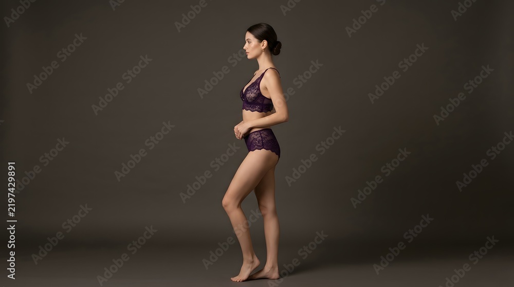 Obraz premium Full body profile shot of a fit woman in dark lingerie against a dark background.