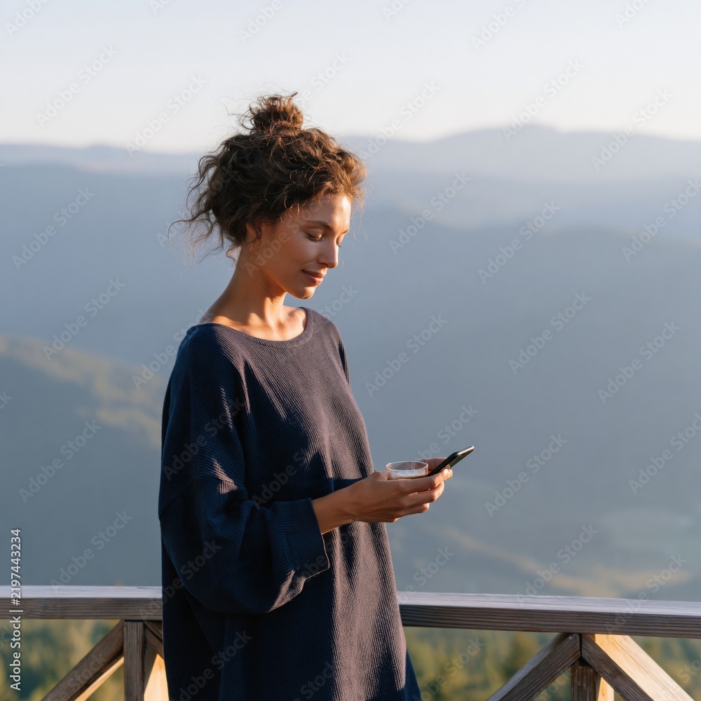 Fototapeta premium Woman on mountain balcony with coffee and phone in the morning for travel blog header and social media background
