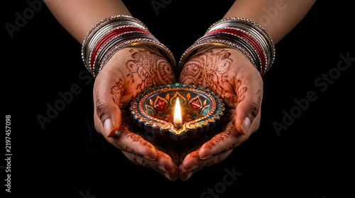 Joyful Diwali celebration with henna adorned hands holding a glowing diya, colorful bangles and intricate rangoli design against a dark background, symbolizing Indian culture, devotion and light