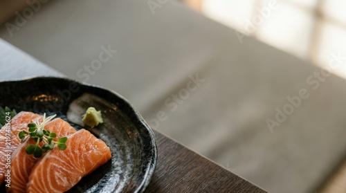 Salmon sashimi on black plate with generous copy space by the window