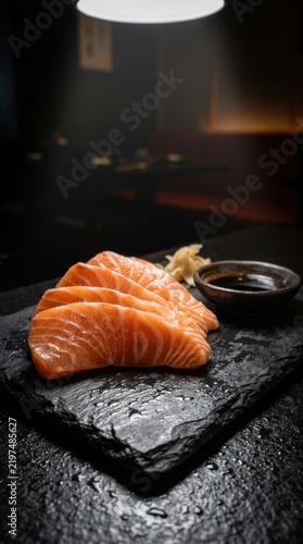 Salmon sashimi on black stone slab under dramatic restaurant lighting