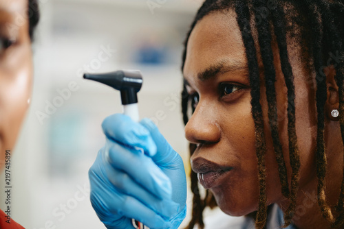 Close up of African American young adult pediatrician examining ear with otoscope during medical checkup. Concept represents pediatric healthcare, suitable for clinic advertising