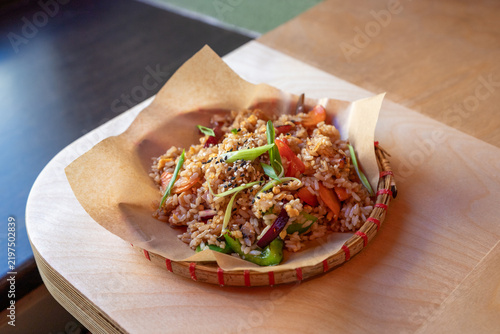 Chicken fried rice with vegetables and sesame fills a paper-lined bamboo basket. Scallion garnish adds color to Vietnamese street food. Asian cuisine concept for a cafe menu.