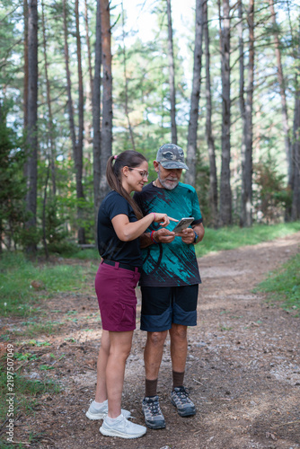 Young woman and senior man looking at a smartphone while hiking in a forest
