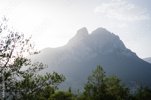Sunlight glowing behind a rocky mountain peak with pine trees in foreground