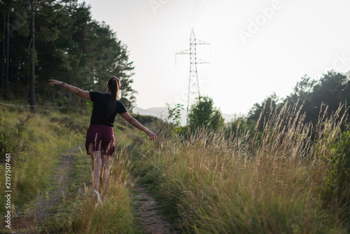 Young woman walking with arms outstretched on a rural path near power lines