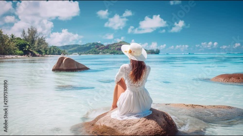 Beautiful woman sitting on a rock in shallow turquoise water looking at a tropical island