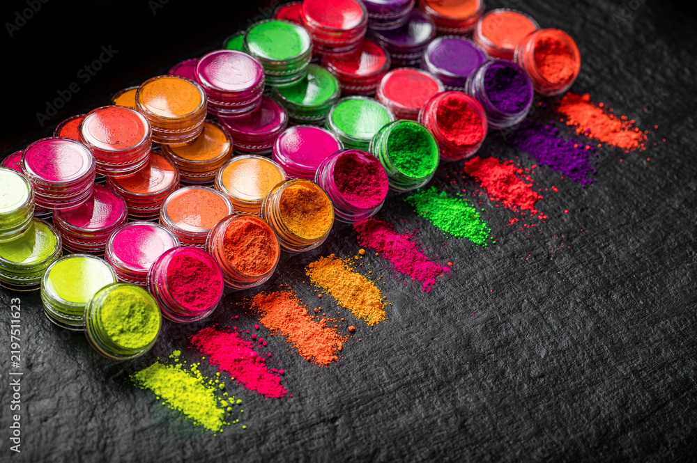 Obraz premium Colorful powdered pigments arranged on a black background with jars and lines of color. Colorful jars of powdered pigments sit side by side on a black surface with lines of color.