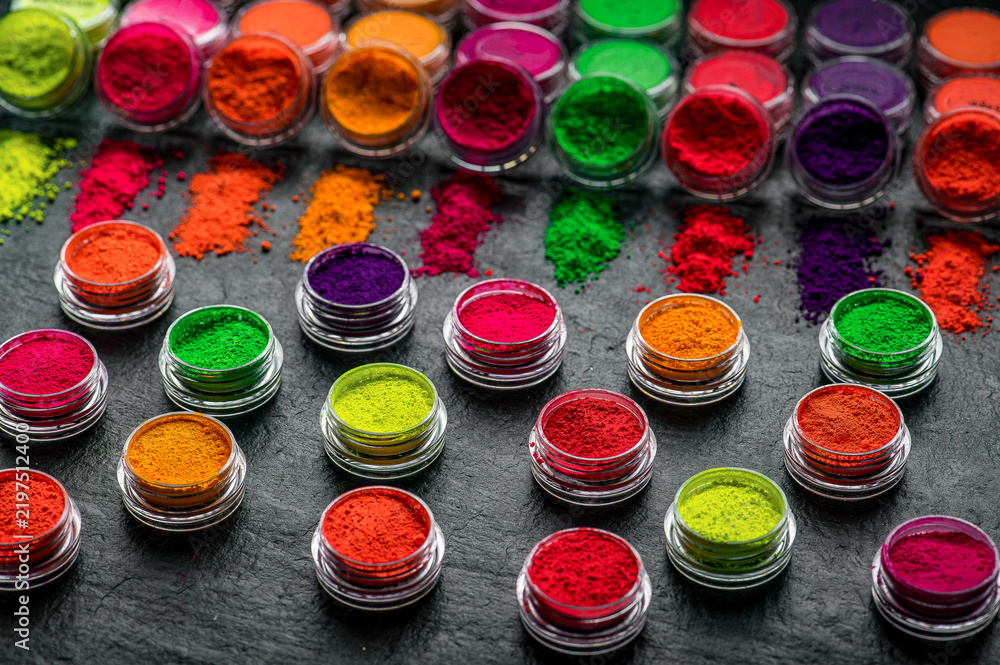 Obraz premium Bright colors of powdered pigments displayed in small jars on a dark surface. Various jars filled with bright powdered pigments are arranged on a dark table surface.