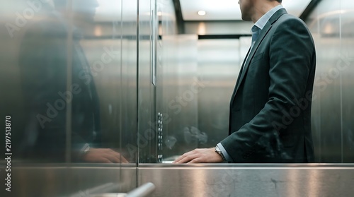 A businessman standing inside an elevator with modern metallic interior walls modern office business suit corporate building business travel man in suit chrome surface work day