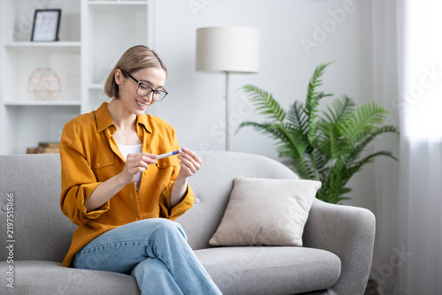 Obraz na plátně Pregnancy test result, happy woman checking medical device at home, family planning and fertility concept, smiling female sitting on a living room sofa, positive news and motherhood anticipation