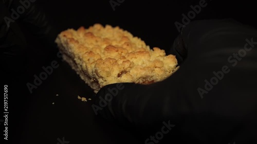 Close-up shot of a chef in black gloves carefully placing a delicious slice of apple crumble bar on a dark background. Ideal stock footage for bakery ads, dessert menus, and commercial food concepts.
